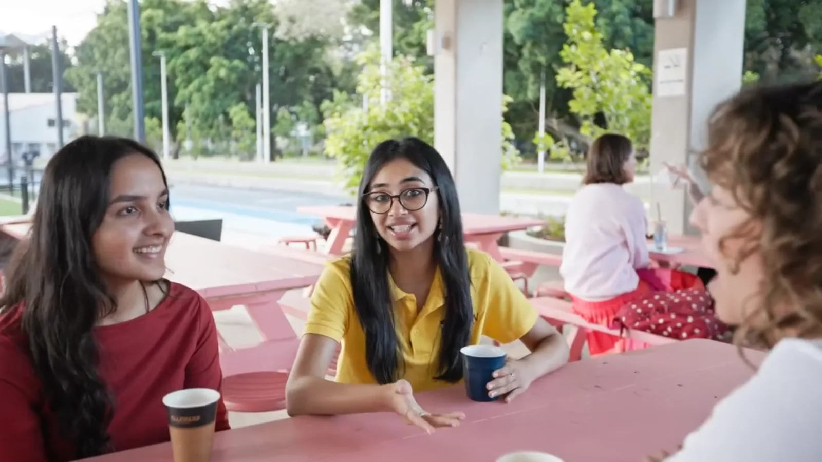 UNSW Gateway student ambassador in a yellow UNSW shirt chatting with high school students at a pink outdoor table on campus